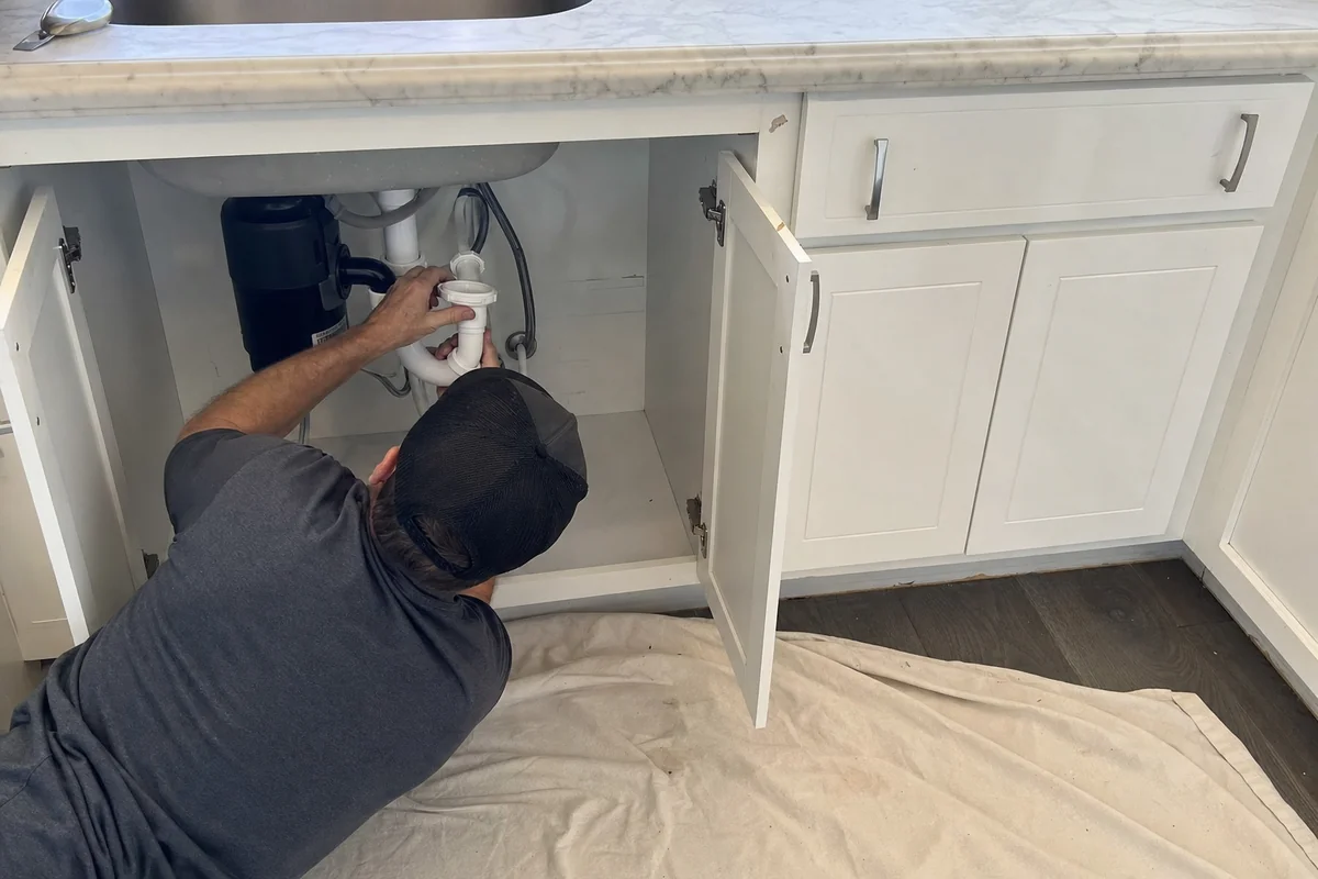 Plumber's hands working on a kitchen sink trap in a Malibu home